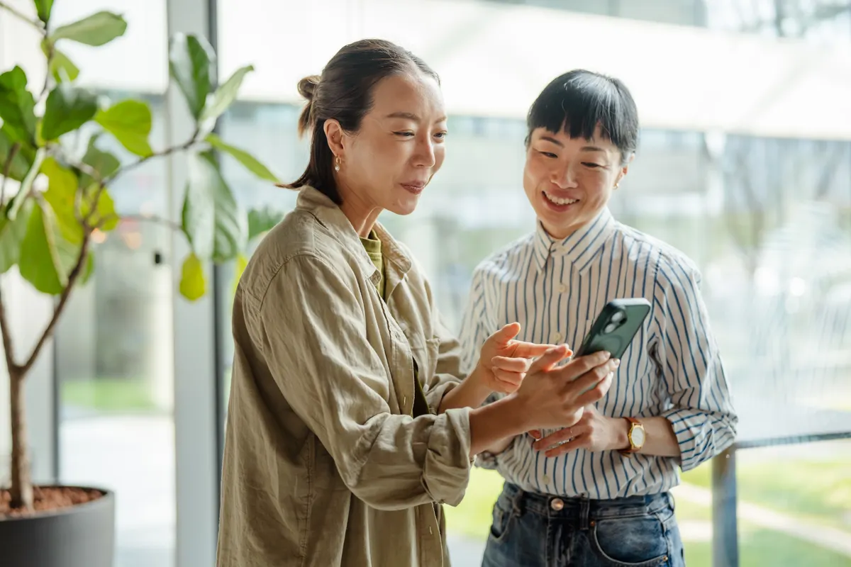Ecommerce conversion rate optimization: two women colleagues communicating using smart phone technology.