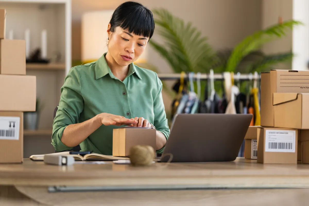 Free shipping threshold: home entrepreneur packing orders at laptop in small business workspace.