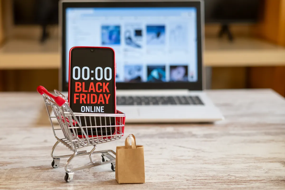 Q4 and black friday ecommerce: shopping cart with smartphone showing black friday online countdown with a laptop displaying an online store in the background represents online shopping and discounts.
