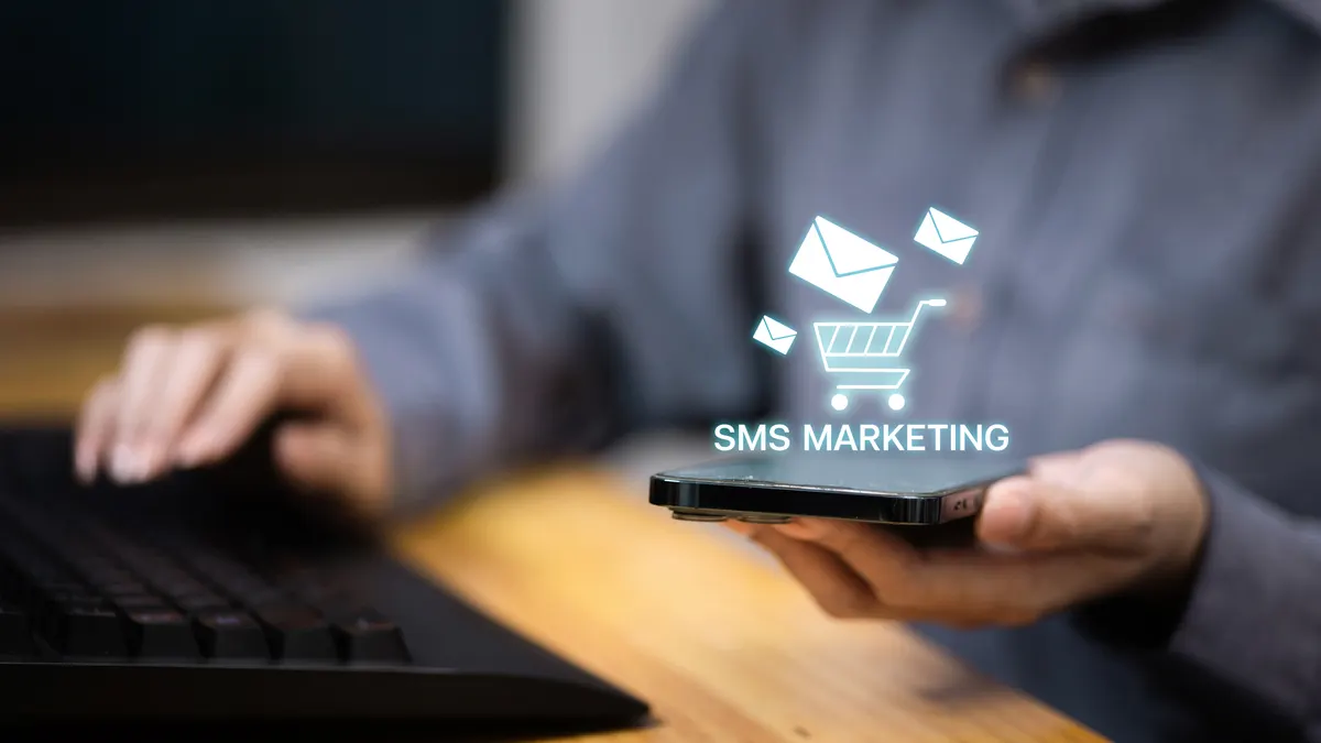 SMS marketing for ecommerce: person holding smartphone with SMS MARKETING text and shopping cart hologram.