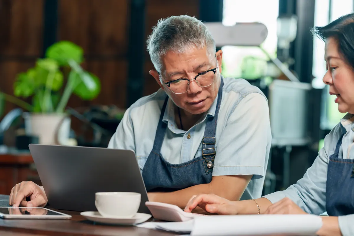 The four lever model: senior asian man cafe owner reviewing data on laptop while woman partner explaining business report teamwork concept small business management communication collaboration entrepreneurship lifestyle.