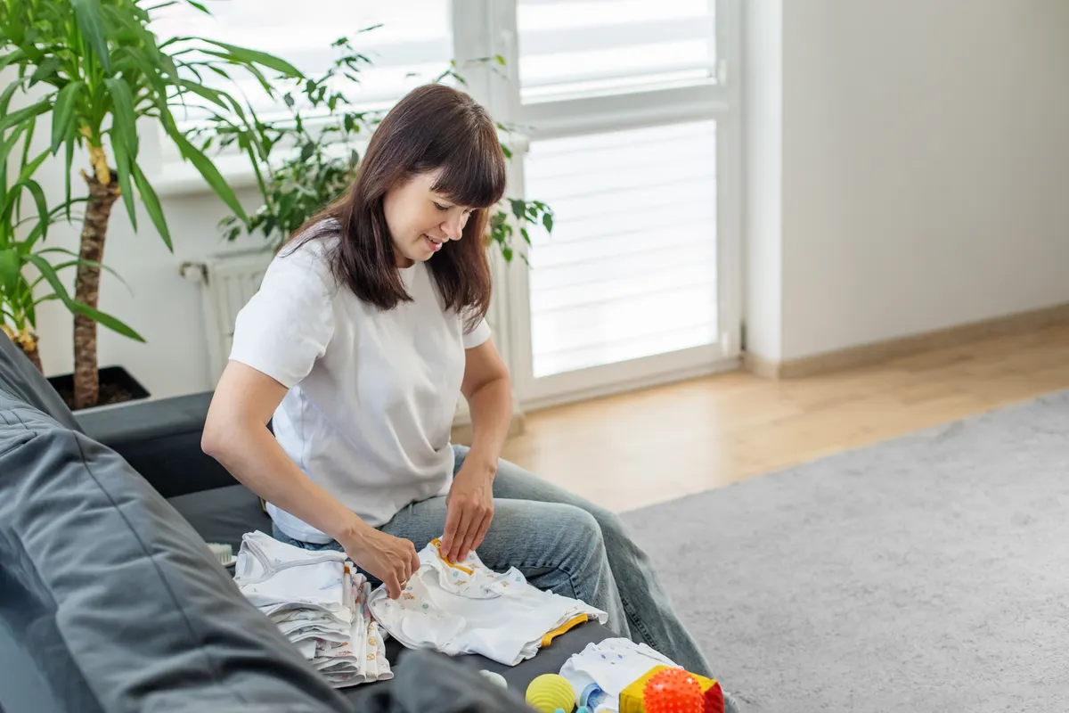 Baby & kids ecommerce marketing agency: happy woman folding baby clothes on sofa.