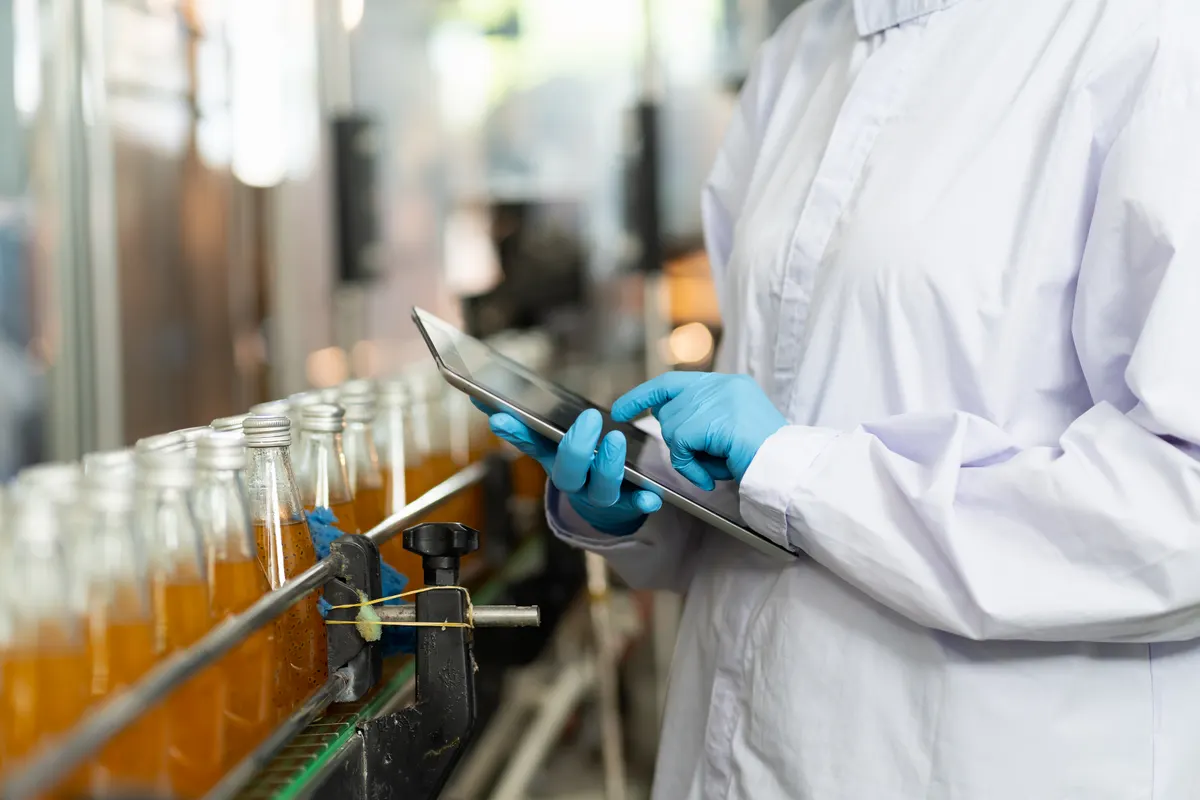 Food & beverage ecommerce marketing agency: hands of worker working with digital tablet check product on the conveyor belt in the beverage factory. Worker checking bottling line for processing. Inspection quality control.