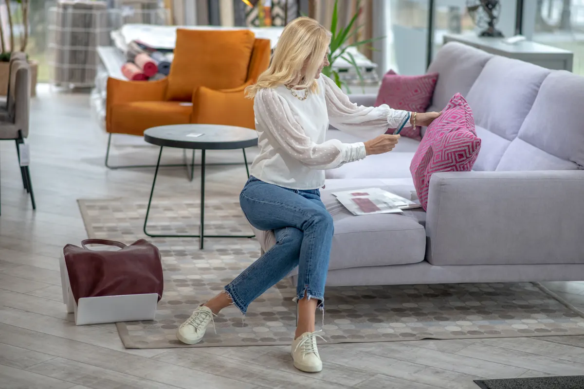 Home & furniture ecommerce marketing agency: woman sitting on a sofa photographing a pink pillow.
