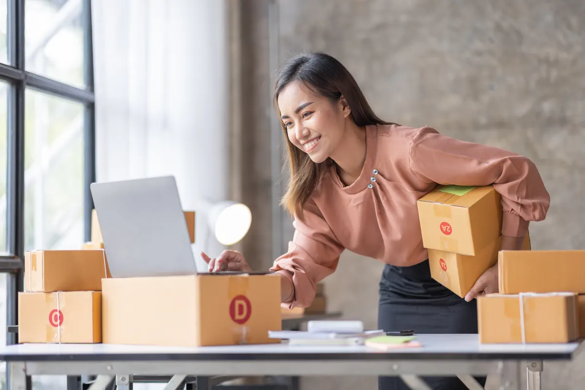 Marketplace seller marketing agency: sME Online seller Young Asian woman working on laptop and box checking online order, check goods stock delivery package shipping postal.