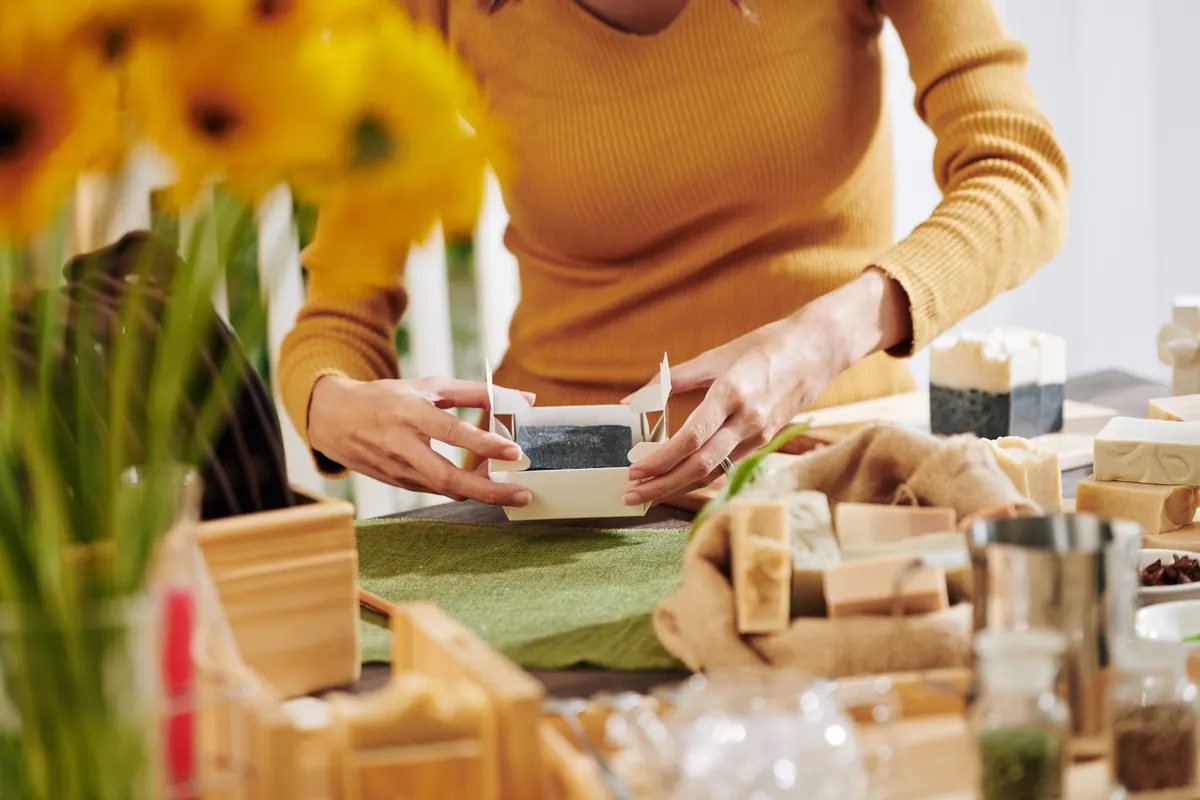 Bundles that raise margin, not just AOV: close-up image of woman packing fragrant soap she made at home in paper box.