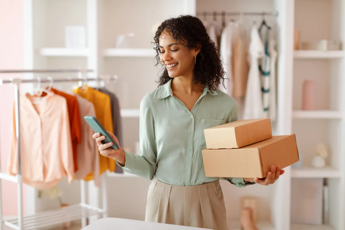 Email list growth without pop-up fatigue: entrepreneur with packages using smartphone in studio.