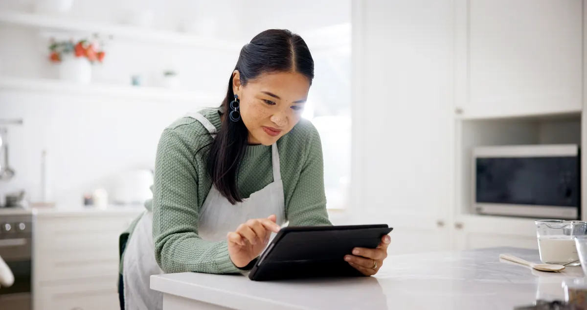 How AI overviews changed product research: cooking, reading and woman with tablet in kitchen, meal inspiration and internet for cuisine tutorial. Research, smile and Asian person with tech for recipe guide, food blog and baking video in home.