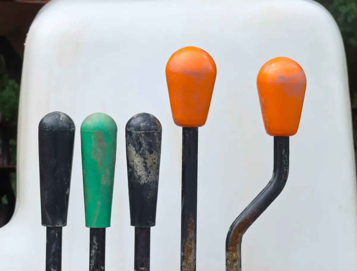 How we choose which lever first: stick shift and four other levers with knobs by molded white seat on earth mover.