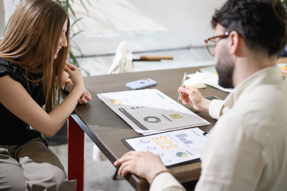 MER vs ROAS: business discussion in a modern office setting with a businessman and a woman engaged in planning and reviewing documents together.