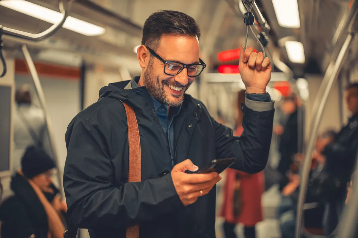 Mobile checkout: a smiling mid adult businessman with glasses using his smart phone while taking a train ride.