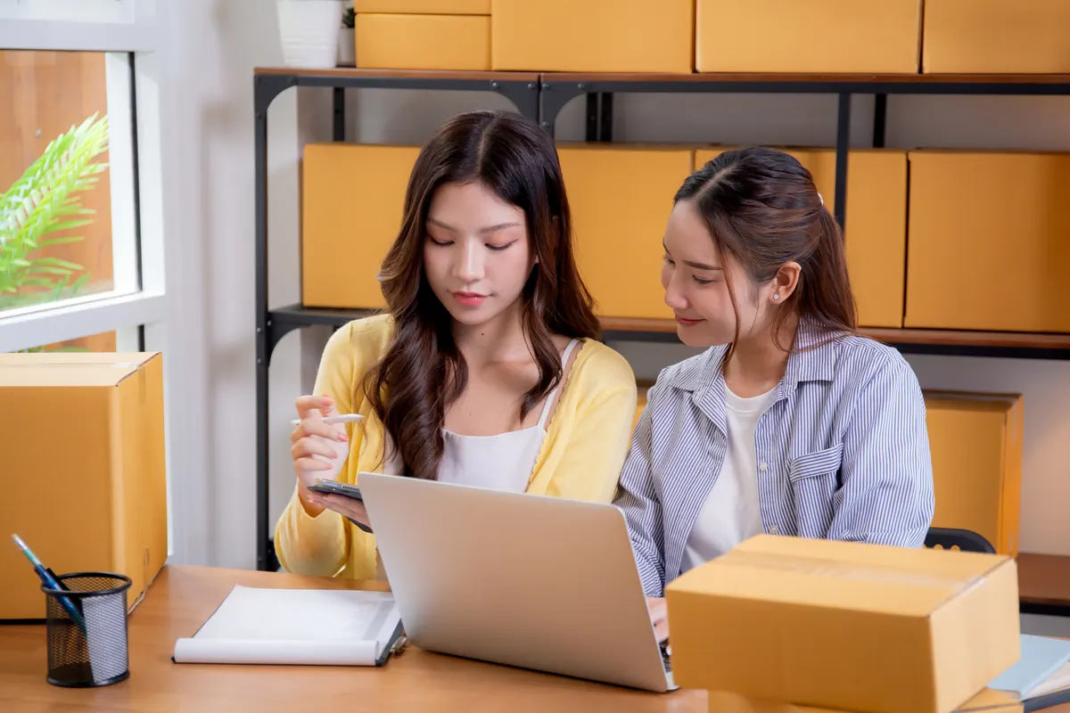 The first three fixes for most stores: two asian young woman merchant checking customer order on tablet and laptop at home office, online seller preparing shipping parcel box with technology for product delivery, small business or startup.