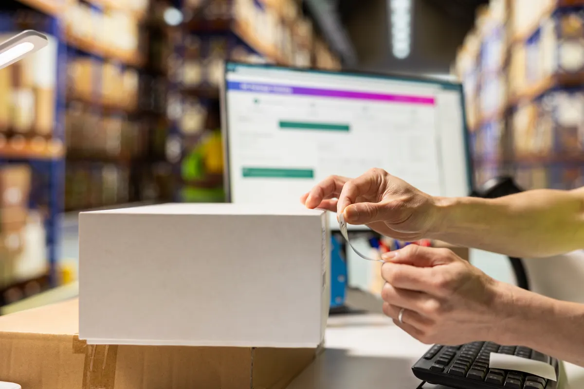 Why product titles matter more than ad copy in shopping: close up of asian worker at packing station applying adhesive airwaybill.