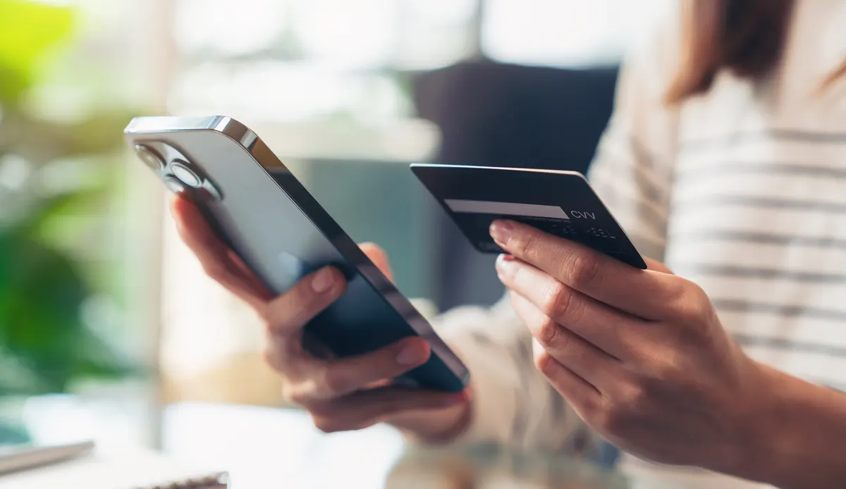 Hands holding a phone and a bank card at checkout