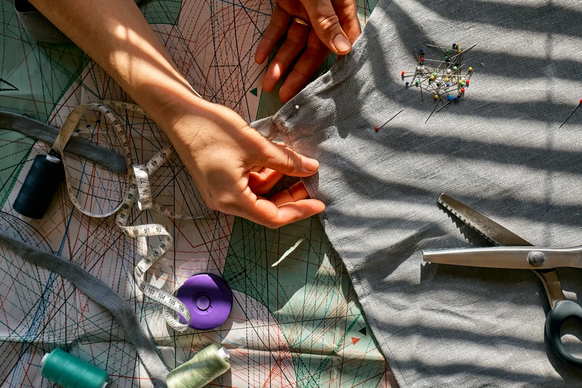 Sustainable fashion marketing agency: woman is sketching pattern on a linen fabric Seamstress basting and sewing in a small studio Sartorial clothes Fashion studio, tailoring, handmade clothing concept Slow fashion Conscious consumption.