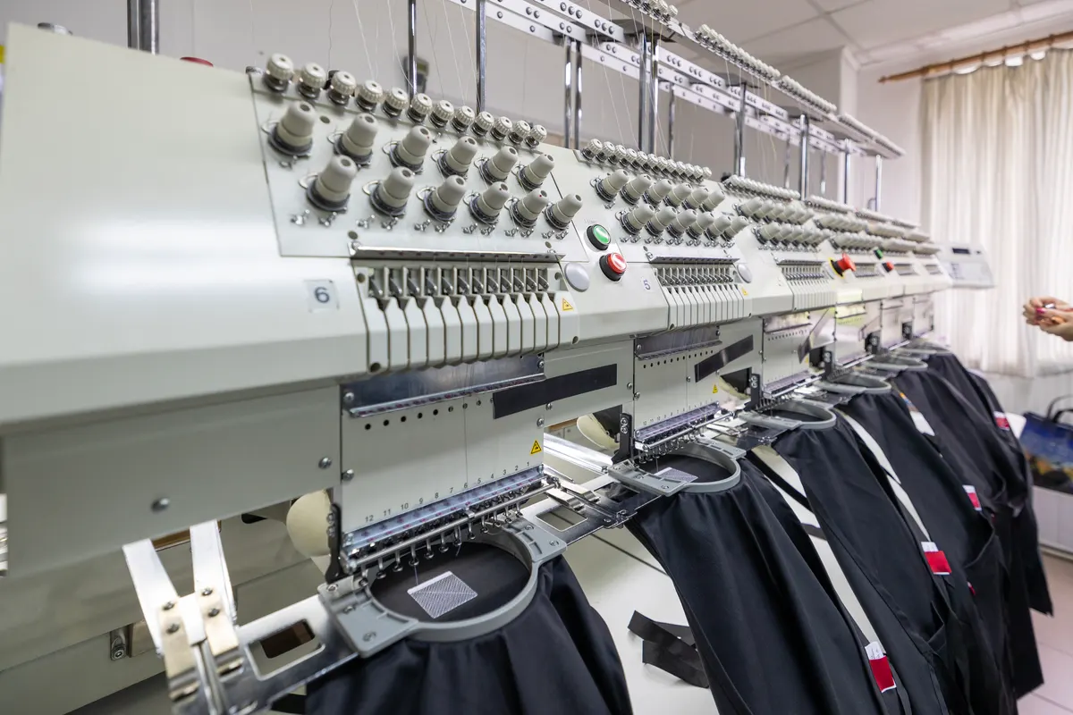 Workwear & uniform marketing agency: professional embroidery machine heads stitching black fabric.