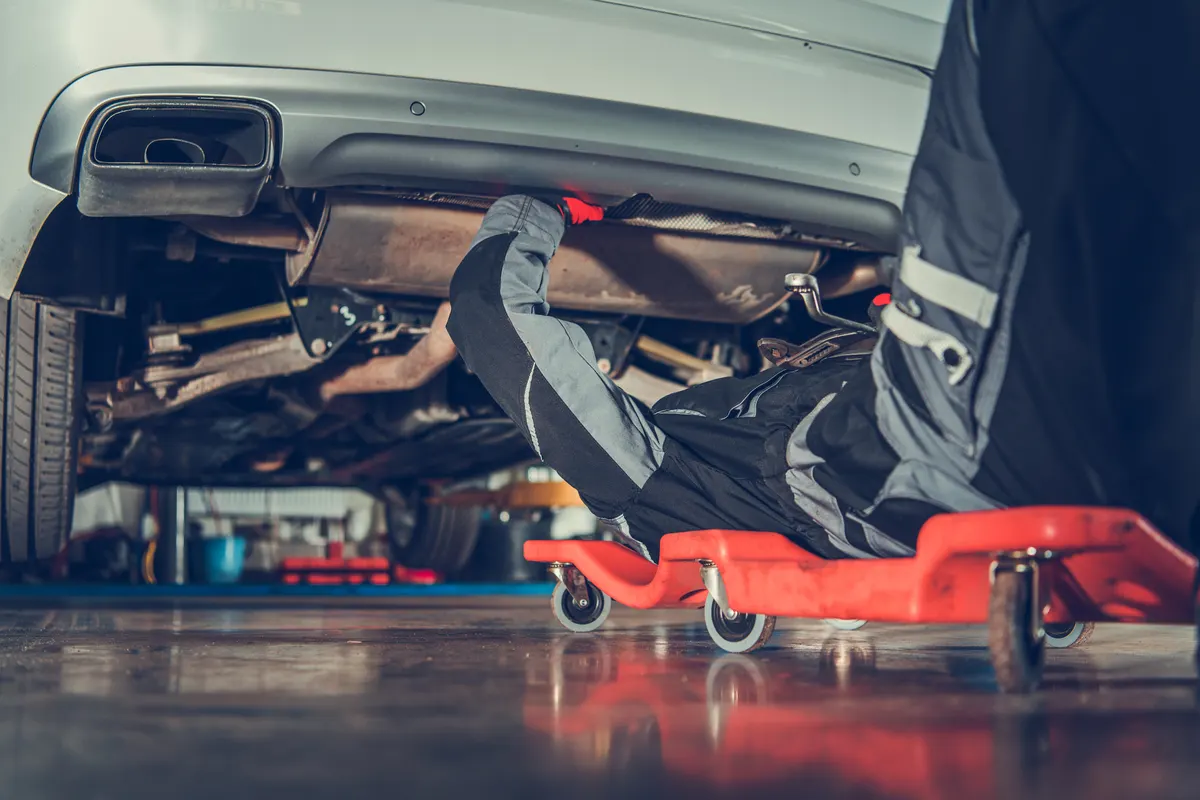 Automotive tool marketing agency: caucasian Vehicle Mechanic in His 30s Repair Vehicle Laying Under Vehicle on the Creeper.