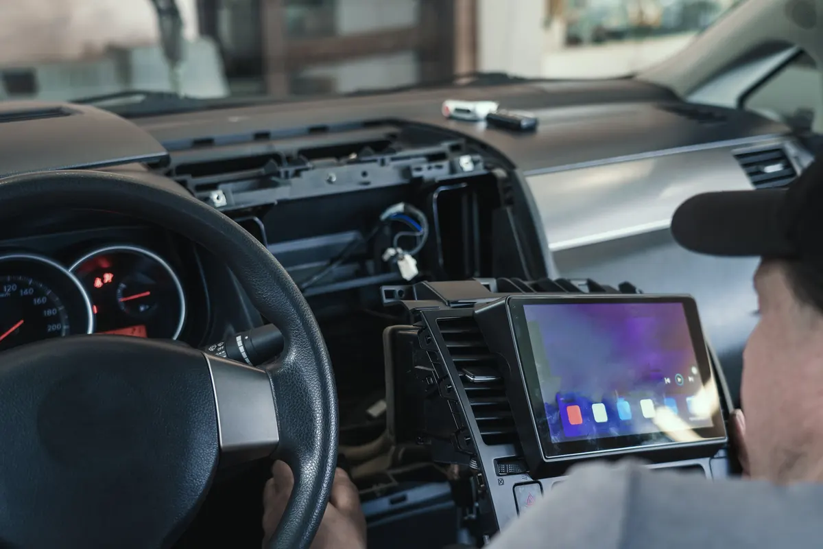 Car audio marketing agency: auto electrician or repairman in car service installs multimedia sound system or car radio in auto dashboard panel.