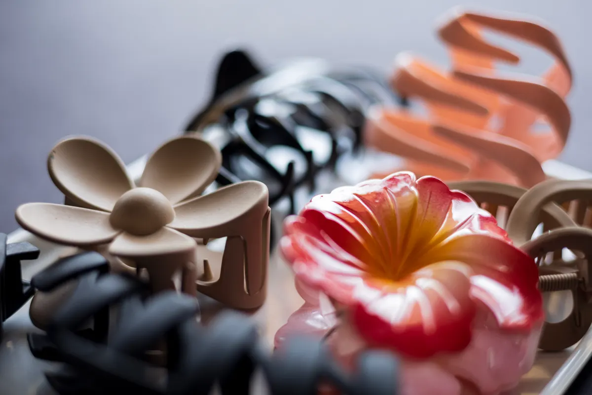 EV accessory marketing agency: a close-up view of various fashionable hair claw clips in different colors and designs on a dark background.