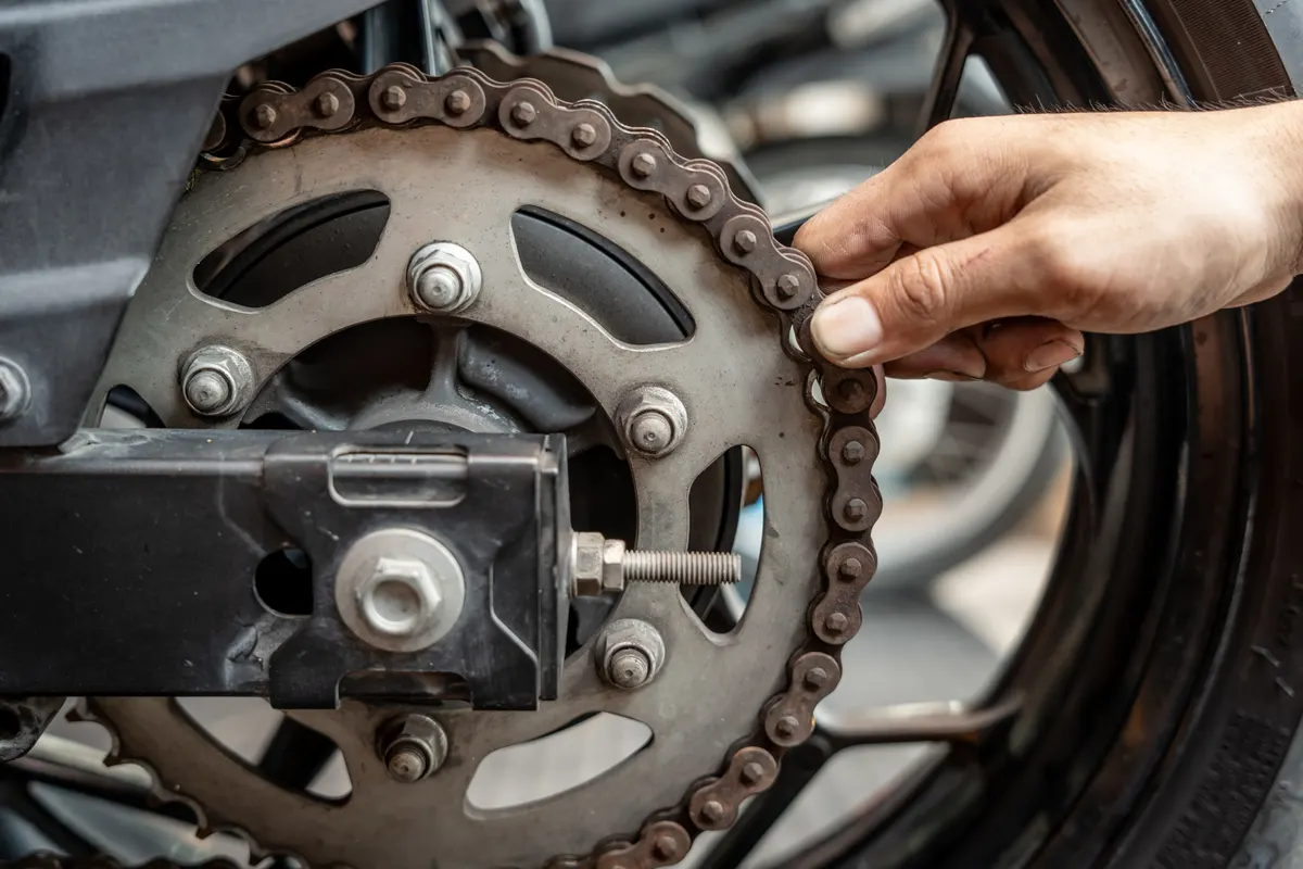 Motorcycle part marketing agency: mechanic Check chain's wear level by attempting to pull it away from the back of the rear sprocket in garage,.