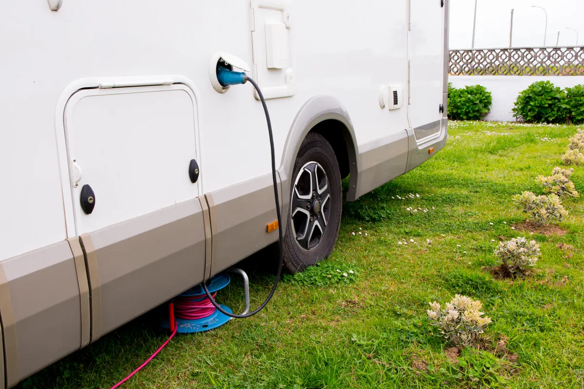 RV & camper accessory marketing agency: camper van power connection on grass with electric cable reel for outdoor use.