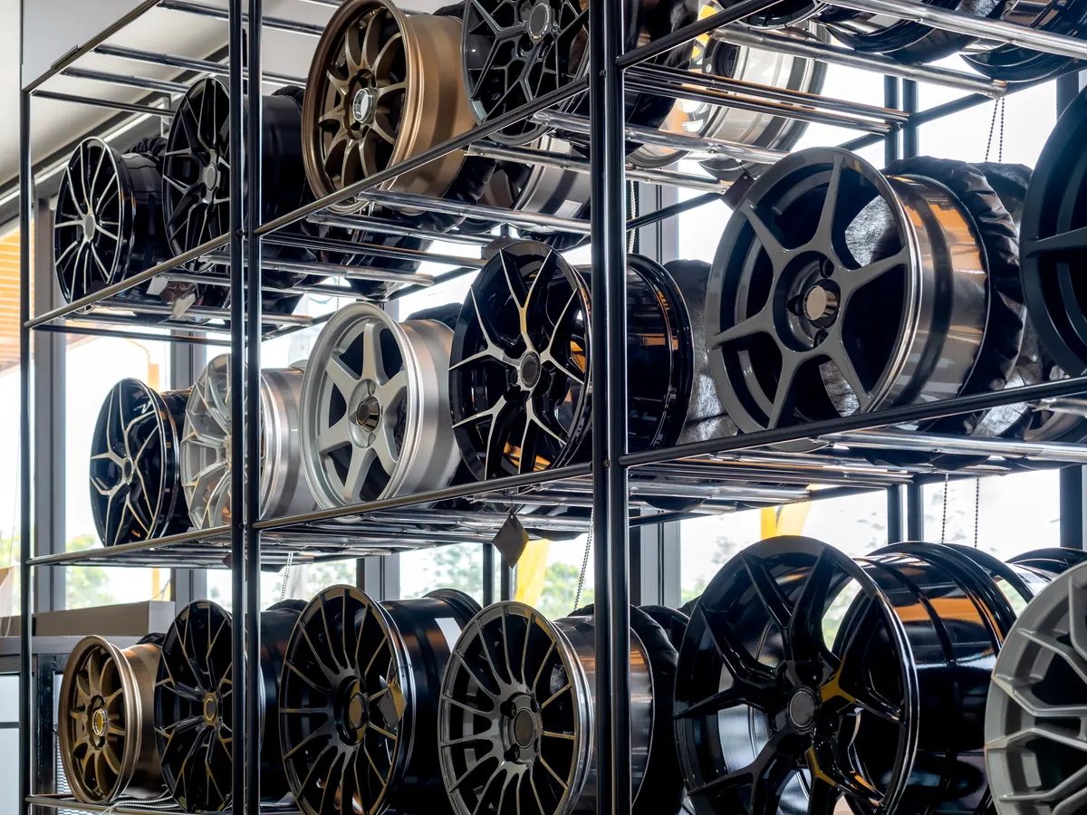 Wheel & rim marketing agency: scene of modern tyre store decoration with various designs of steel alloy wheels rim on metal shelf inside the building near huge glass window. Alloy wheel showroom shop background.
