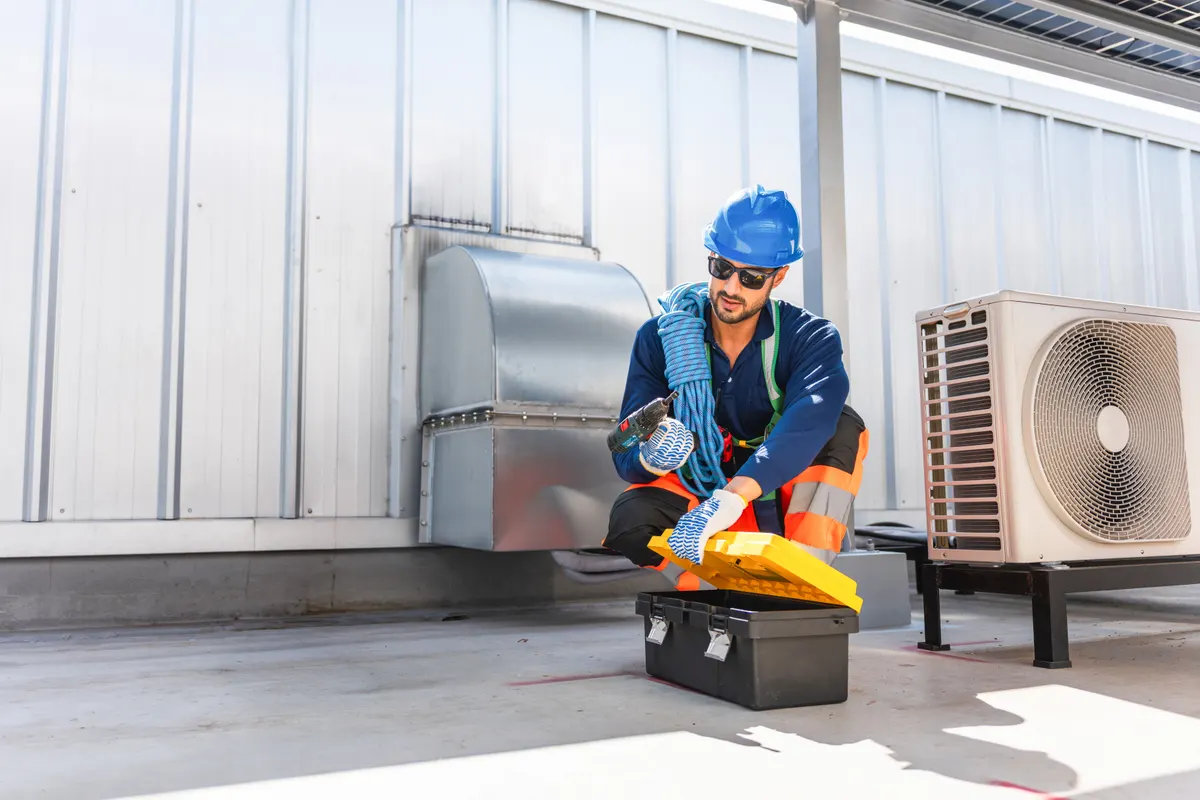 HVAC part marketing agency: technician man taking electric drill from toolbox for hvac maintenance, Maintenance worker preparing tools on rooftop, Service engineer in safety gear repairing industrial air conditioning unit.