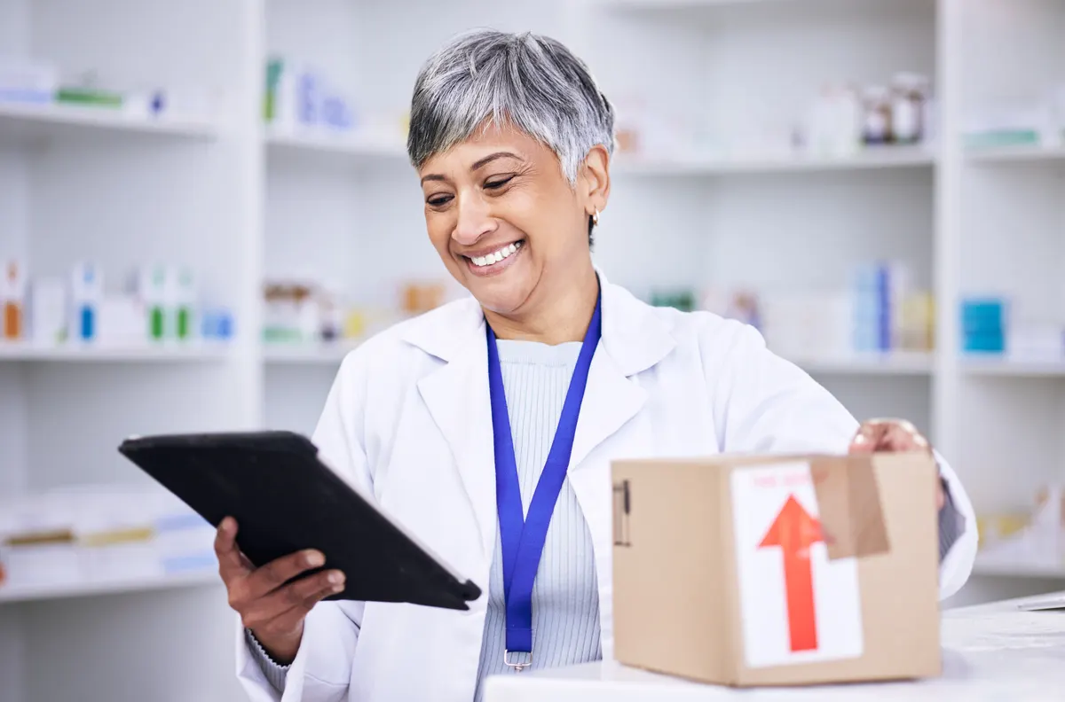 Medical supply marketing agency: happy woman, pharmacist and tablet in logistics with box for online order, delivery or shipping at pharmacy. Senior female person in medical healthcare for ecommerce or pharmaceuticals on technology.