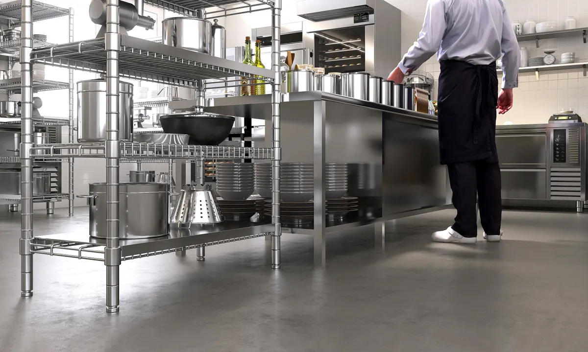 Restaurant supply marketing agency: male professional chef baker working in commercial bakery kitchen on stainless steel table counter, shelf with machine, equipment in sunlight from window on vinyl floor.