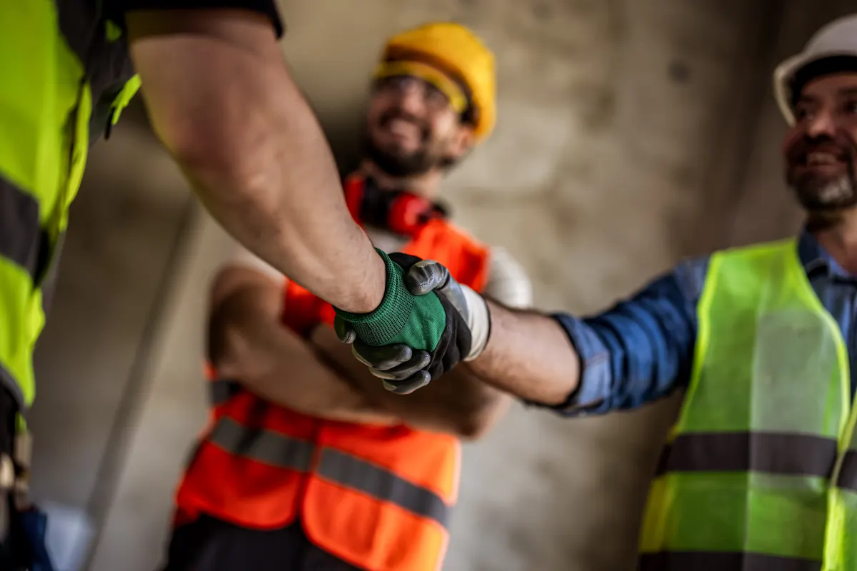 Safety & PPE marketing agency: close-up of construction workers shaking hands on a building site.