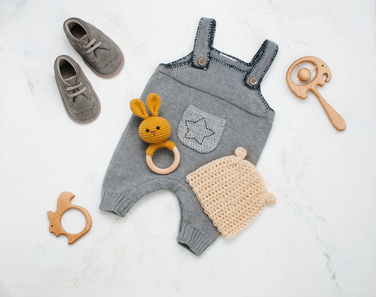 Baby clothing marketing agency: newborn baby clothing and beanbag on light marble background.