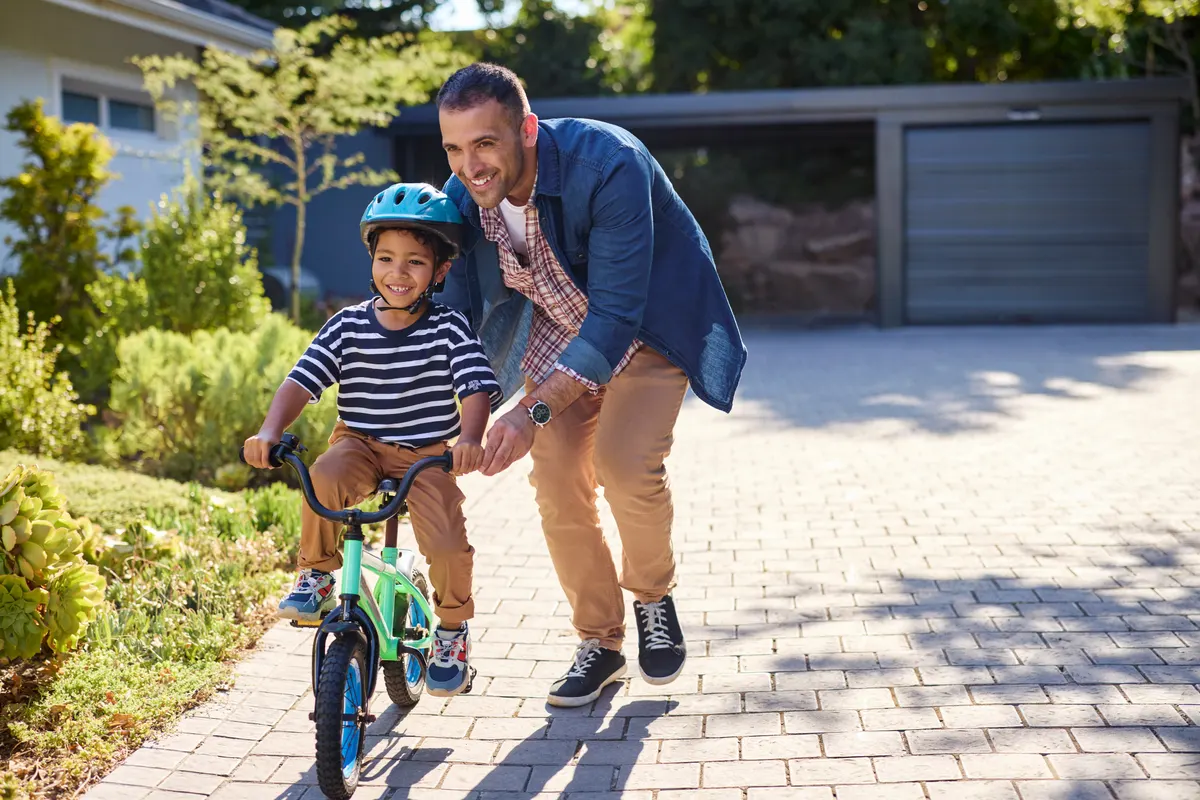 Kids' bike & ride-on marketing agency: happy smiling father helping son riding bike outdoor.