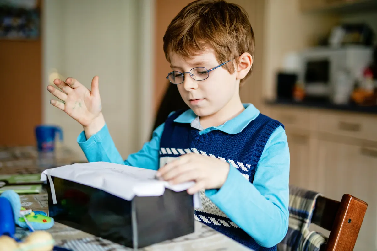Kids' book subscription marketing agency: happy little kid boy doing school homework. child with eye glasses making a box at home. Creative activity for kids.