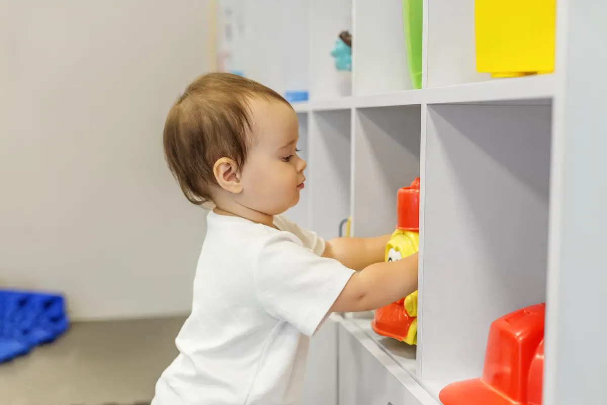 Montessori toy marketing agency: toddler Choosing Toy From Storage Shelf During Independent Play at Daycare.