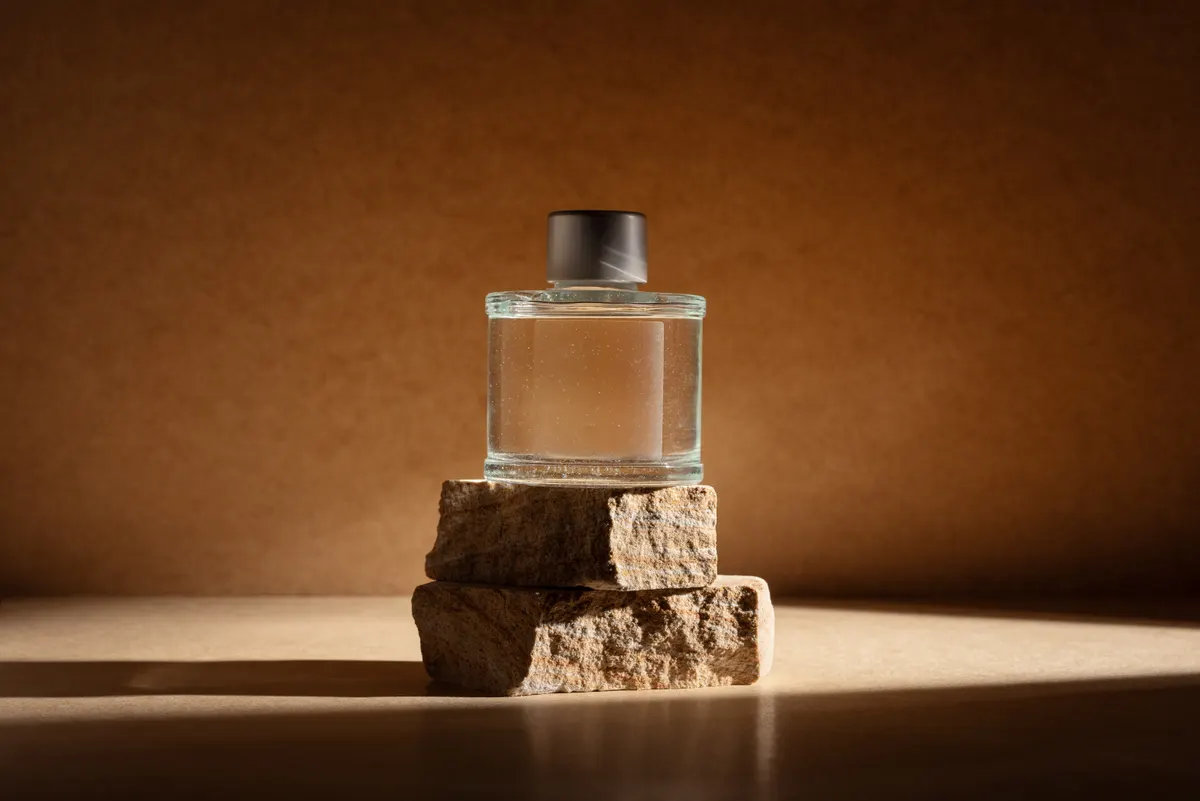 Fragrance marketing agency: glass perfume bottle or home fragrance on natural stone podium in dramatic light.