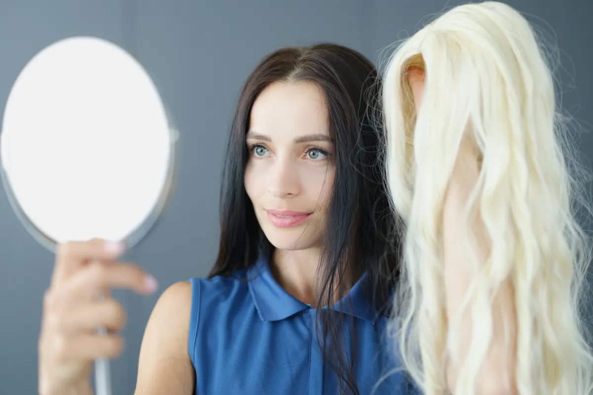 Hair extension & wig marketing agency: young brunette woman holding white wig in front of mirror.