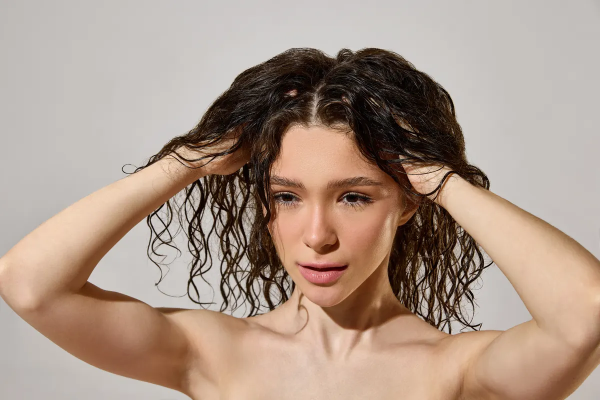 Haircare marketing agency: woman massaging wet curly hair roots during moisturizing hair care routine.