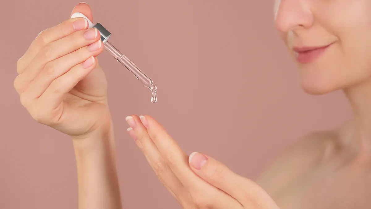 Skincare marketing agency: close-up of female hands on pink background holds dropper facial serum ads.