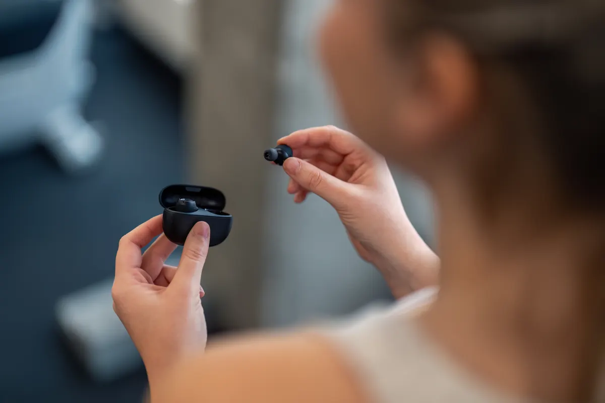 Audio & headphone marketing agency: close up photo over woman's shoulder of woman's hands holding black earphones.