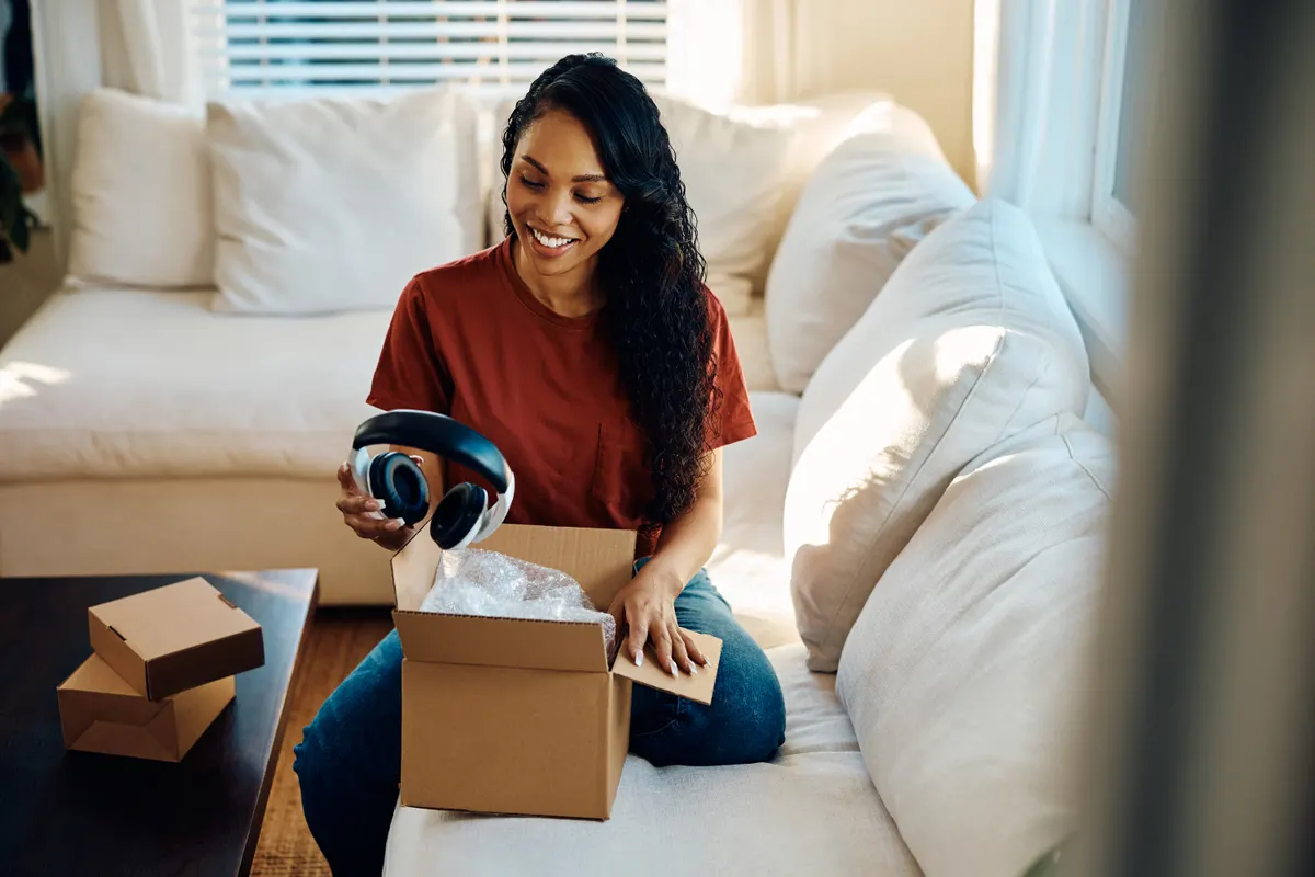 Consumer electronics marketing agency: happy black woman unpacking new headphones she bought online.