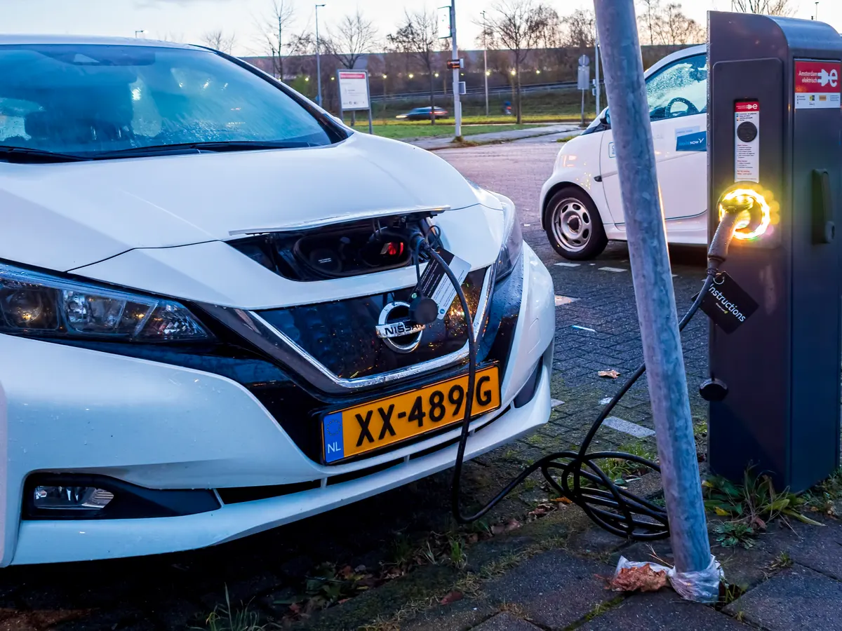 EV charger marketing agency: small size white electric Nissan vehicle in a parking lot being charged.