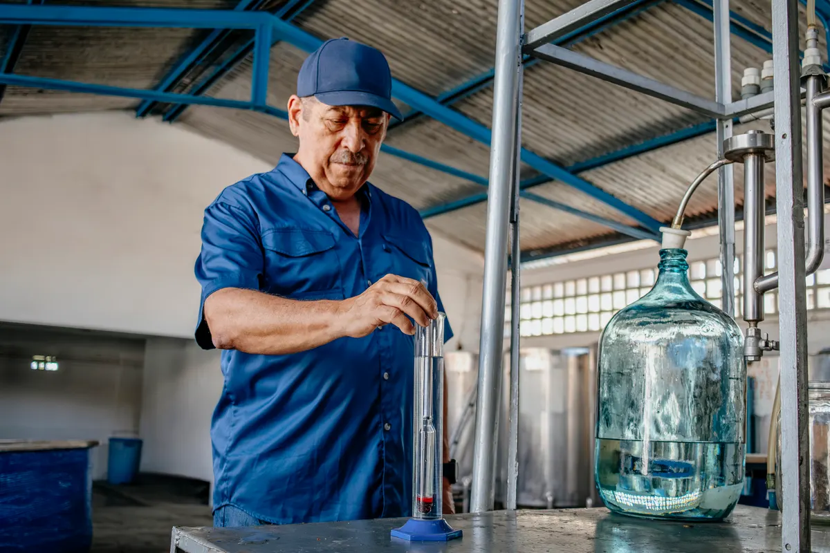 Craft spirit marketing agency: distillery worker testing alcohol levels with a glass hydrometer tube.
