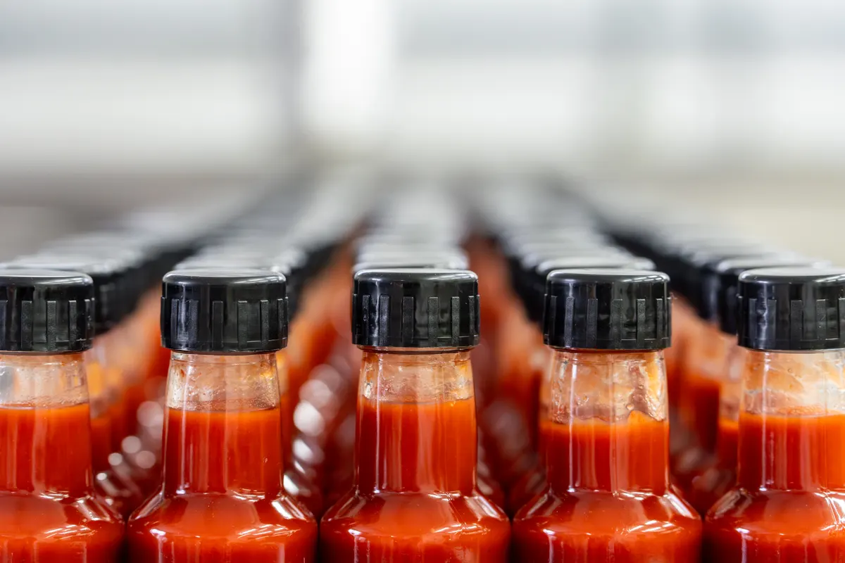 Hot sauce marketing agency: rows of red hot sauce bottles waiting on conveyor belt.