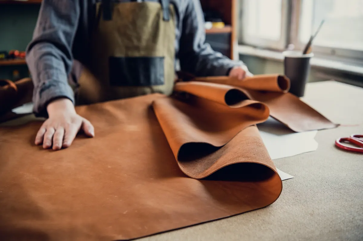 Boot marketing agency: a young apprentice in a boot workshop prepares leather for further use on a large table.