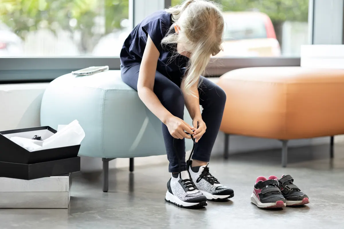 Kids' shoe marketing agency: kid tying her shoelaces and trying on sport shoes in store.