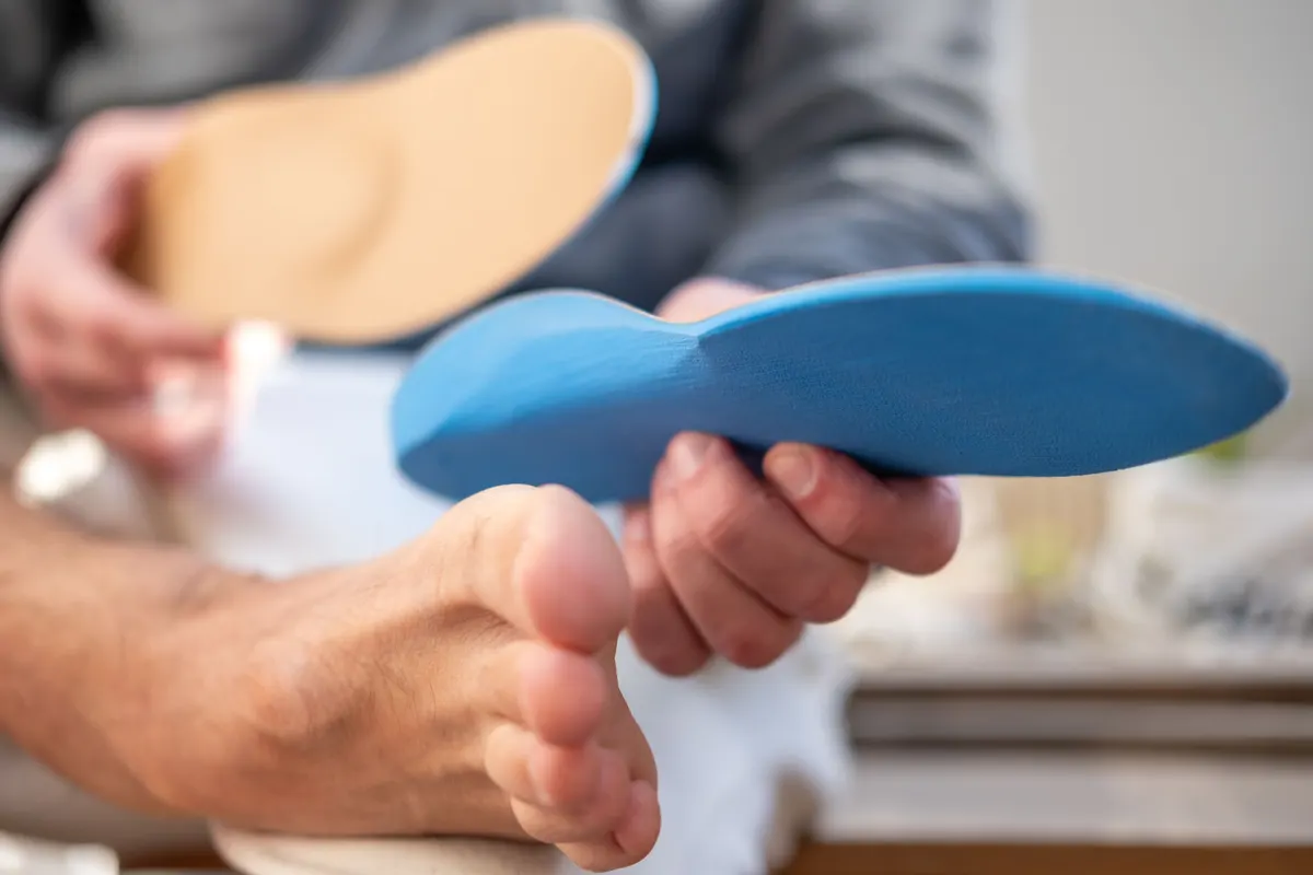 Orthopedic & comfort shoe marketing agency: man trying orthopedic shoe insoles on bare foot, fitting medical arch support insert, Podiatry and foot health prevention, foot care and podiatry concept, choosing comfortable support for walking.