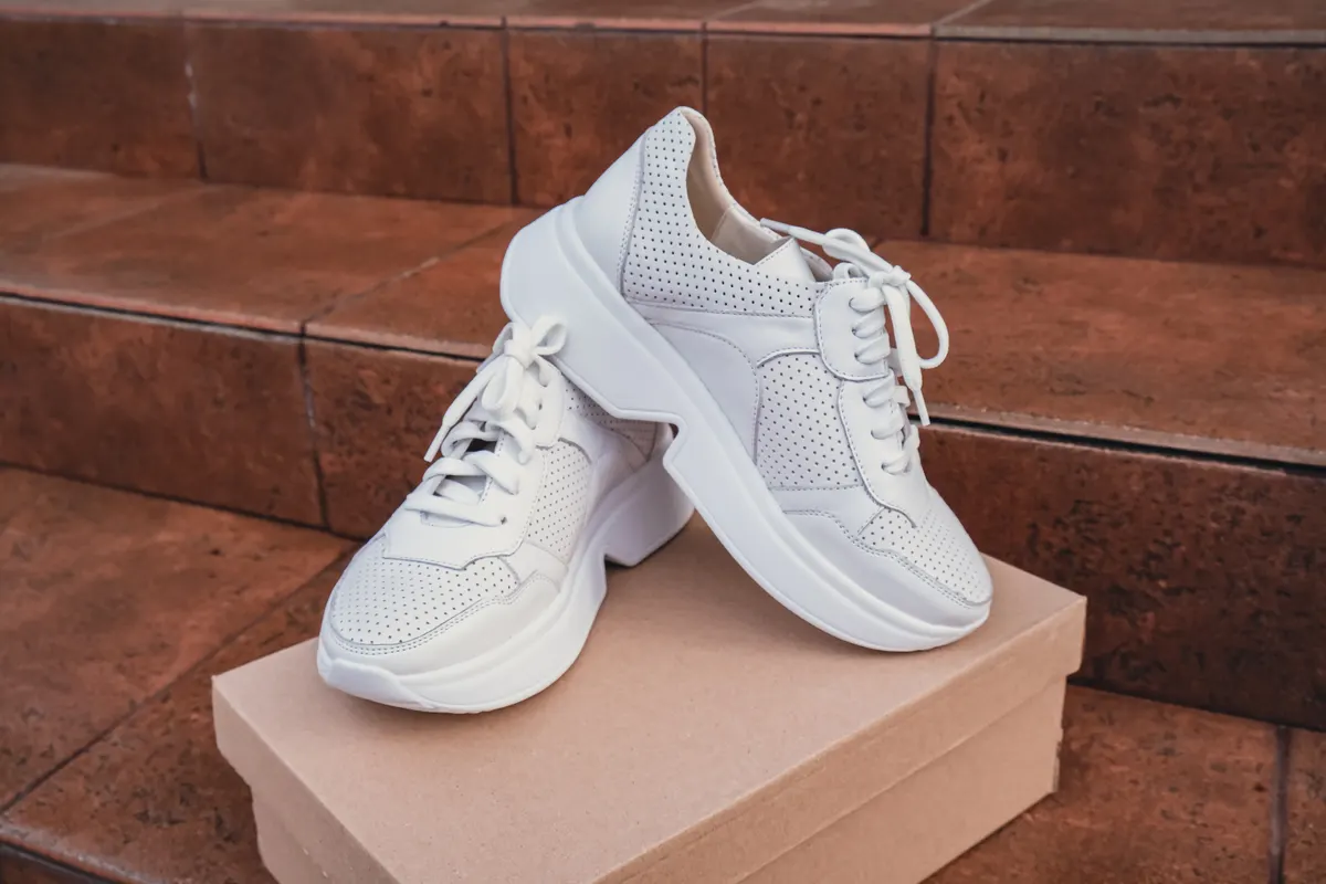 Sneaker marketing agency: minimalist eco-friendly white sneakers placed on recycled cardboard box, clean design for sustainable fashion concepts. New unbranded white sneakers footwear mockups and modern product displays. For branding, e-commerce.