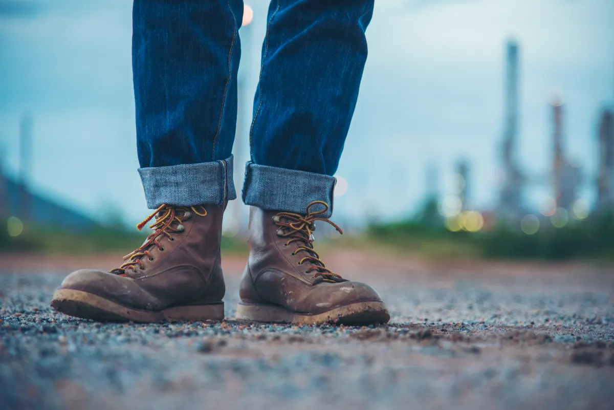 Work boot marketing agency: men wear construction Boots safety footwear for worker at construction site. Engineer Wear Jeans Brown Boots Worker on Background of Refinery. Engineer safety industry fashion footwear walking outdoor.