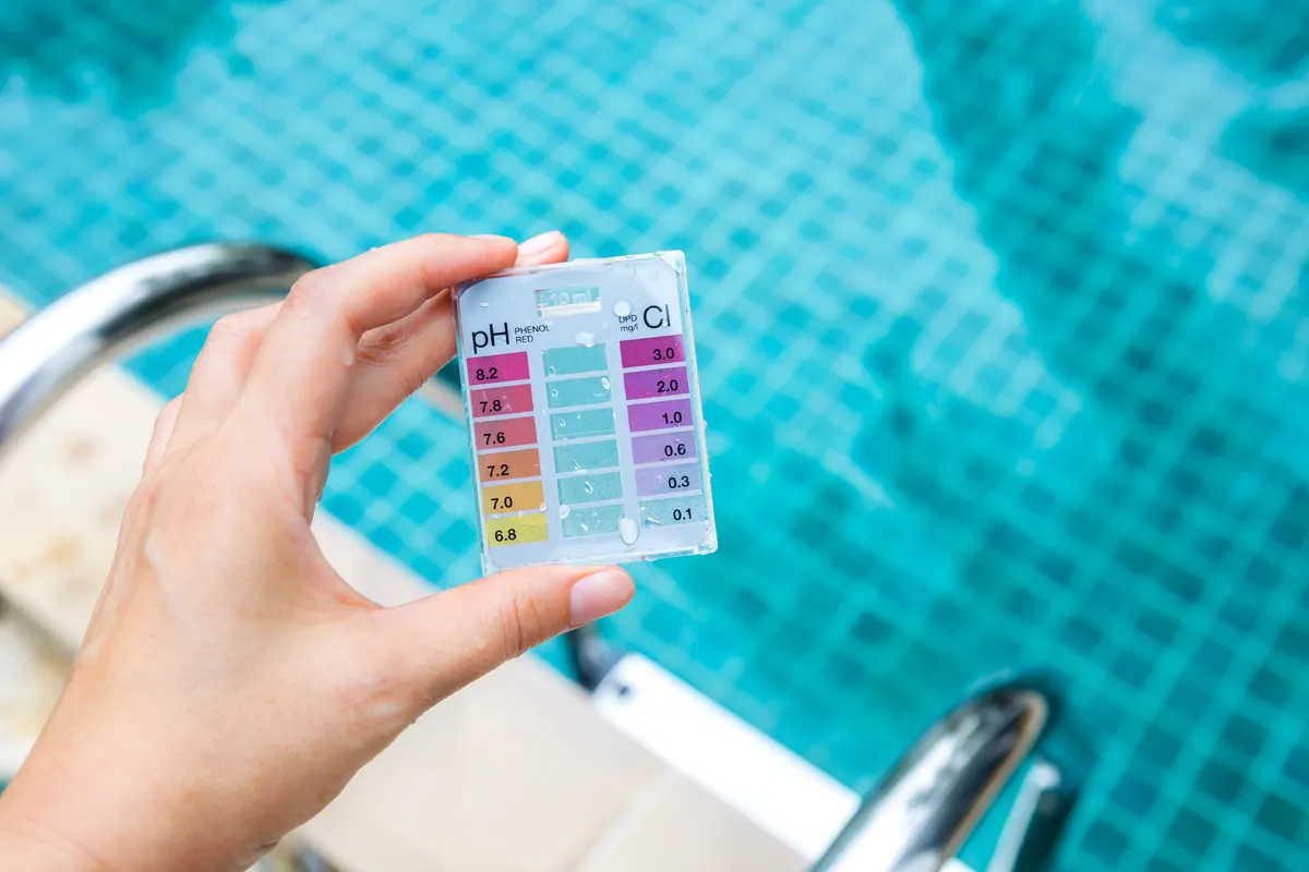 Pool supply marketing agency: girl hand holding mini water testing test kit over blurred swimming pool background.