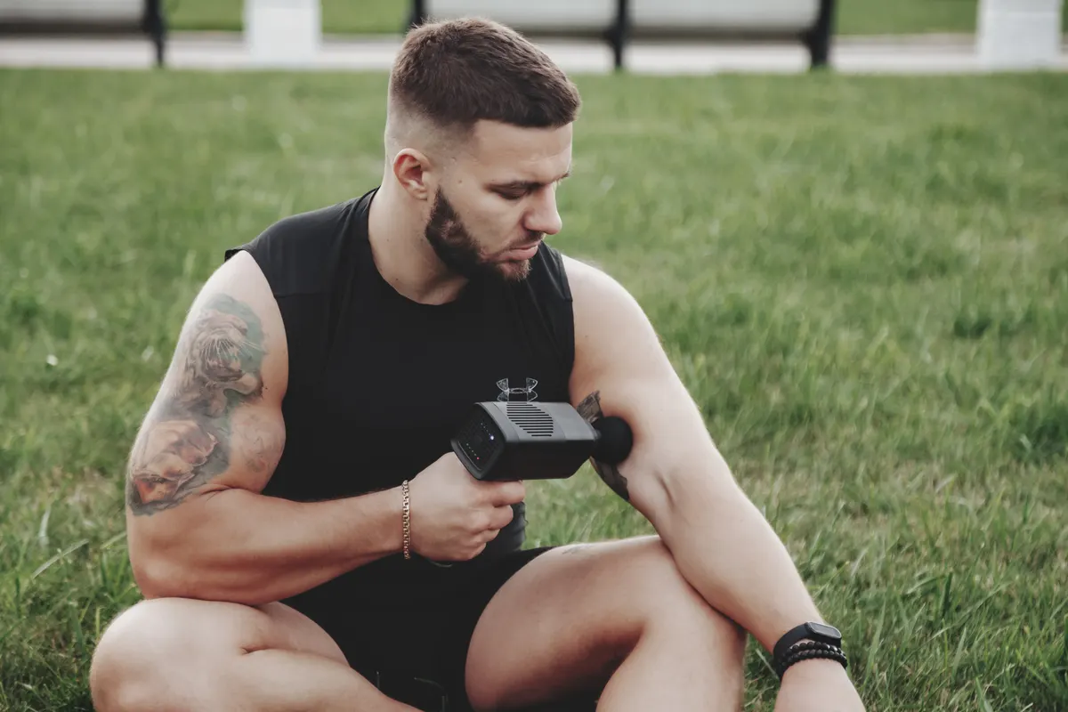 Massage & recovery device marketing agency: man massages body with massage percussion gun device.